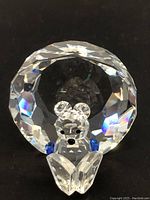 Front angle of clear faceted Swarovski crystal bear reading a book with blue paws and black eyes and nose.