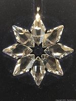 Clear Swarovski crystal star-shaped ornament with 8 faceted points and gold-tone hanging loop, shown against black background.