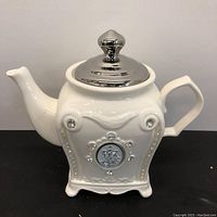 Full view of the white Verdici Design teapot showing its shape, silver lid, and rhinestone embellishments.