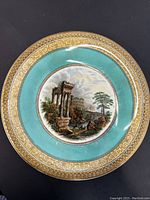 Front view of the plate showing the scenic ruin motif with turquoise and gold border.
