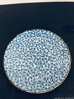 Top-down view showing the intricate white swirling vine pattern on a rich blue background with a scalloped gold rim.