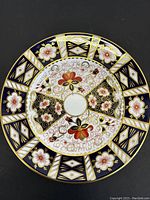 Front view of the plate showing intricate floral and geometric patterns with gold detailing on navy blue and white background.
