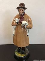 Front view of the vintage Royal Doulton Lambing Time figurine showing the elderly woman holding two lambs and standing on a grassy base.