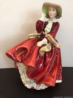 Front view of the Royal Doulton figurine showing the woman's seated pose, red dress with ruffles, and wide-brimmed hat detail.