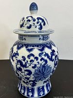 Front view of vintage blue and white Asian jar with lid, showing floral vine motif and rounded finial on top.