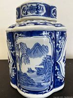 Front side of the blue and white porcelain jar showing scenic landscape painting with trees, waters, mountains, and boats.