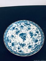 Top-down view of blue grape and floral motif on vintage round scalloped Asian plate.