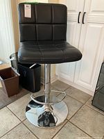 Front and side view of the black leatherette bar stool showing the padded seat, square stitching detail, chrome base and circular footrest.