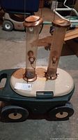 Two copper-topped cylindrical bird feeders placed on the beige perforated lid of the plastic wheeled cart in a basement setting.