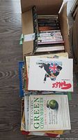 Photo showing packed box of books with multiple titles including a satirical title featuring a British flag on animal artwork, 'Green Consumer Guide' by Julia Carabias, and other assorted books.