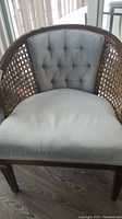 Front view of vintage chair showing light blue-grey fabric upholstery with tufted backrest and caned wooden sides.