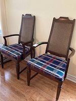Two wooden Gibbard captain dining chairs with cane backs and plaid cloth upholstered seats, showing full view of both chairs in room setting.