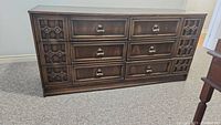 Full view of vintage wooden dresser with 6 drawers showing carved side panels and metal ring handles.
