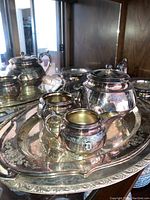 Overview of silver plated tea set on a large ornate serving tray showing teapot, cream pitcher, sugar bowl, and serving dishes with visible monogram.