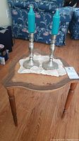 Wooden side table with two pewter candlesticks holding blue candles displayed on top, set on wooden floor.