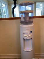 Full view of Vitapur water cooler with water reservoir tank on top sitting in a room near windows.