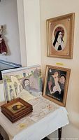 Four wood-framed signed fruit-themed pictures, one oil painting on canvas of street scene, and two religious-themed framed prints displayed on a table and wall.