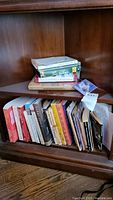 Shelf with approximately 17 books arranged vertically and partially horizontally with documents and a small card.