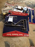 Photo showing door and chain locks along with ornamental hanger brackets in packaging arranged on carpet