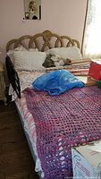 Full view of the bed with headboard, bed linens, and various items on top illustrating condition and materials