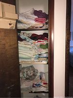 Three-shelf linen closet filled with folded towels, tablecloths, sheets, and napkins