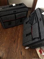 Two rolling suitcases by Givenchy in grey textured fabric with black and red trim, shown standing on a hardwood floor