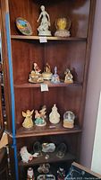 Wooden shelves with five layers holding various ceramic and resin decorative items including snow globes, figurines, music boxes, and candle holders arranged with some showing tags.