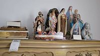Shelf with assorted ceramic nativity figures, religious books, and wall art.