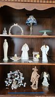 Overview of nativity and angel figurines on shelves alongside stained glass tea light lamp and floral tree sculpture