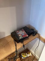PlayStation 2 console with wired controller and Grand Theft Auto 3 game case on wooden surface
