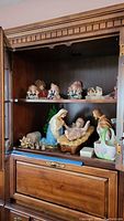 Porcelain doll figurines and ceramic nativity set displayed inside wood cabinet
