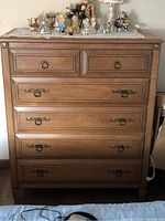 Six drawer wooden dresser with brass accents and metal handles, showing wear and small decorative objects on top.