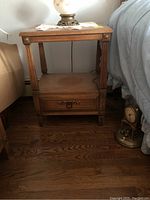 Full view of one wooden nightstand showing top surface, lower open shelf, and drawer with brass hardware.