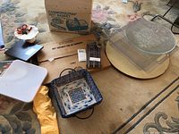 Overview of all items including the boxed Salton Cosmopolitan hot basket, ceramic dishes, candle snuffers, and candle on the floor and a rug.