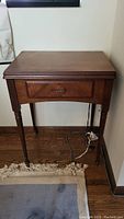 Full view of the closed wooden sewing machine cabinet showing front drawer and legs with some wear.