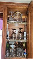 Shelf with clear, brown, and yellow stemmed glasses, clear glass jar with lid, and white ceramic stemware with blue and red designs.