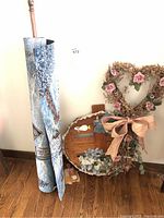Rolled tapestry leaning against the wall next to dried flower heart-shaped wall art with ribbon bow