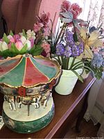 Photo of the Thomas Kincaid Victorian carousel showing top portion and some artificial flower arrangements behind it.