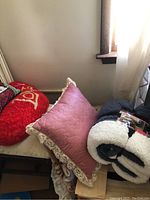 Shows pink and red decorative pillows next to two rolled sherpa throw blankets.