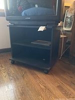 Front view of the black wooden TV stand showing two open storage shelves and caster wheels.