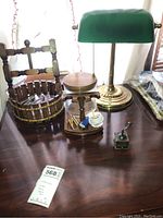 Photo showing vintage green-shade brass desk lamp, brass phonograph replica, and wooden decor pieces on a wooden table.