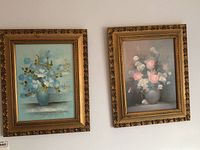 Photo of two framed floral paintings side by side, showing flower arrangements in vases with ornate gold frames.