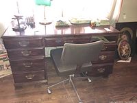 Full view of hardwood writing desk with brass drawer pulls and canvas swivel chair on wheels