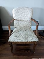 Front view of the antique upholstered wooden armchair showing patterned fabric seat and backrest and curved wooden arms.