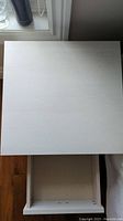 Top view of the bedside table showing the whitewashed surface and open drawer interior.
