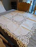 Square white cotton lace tablecloth spread on a dining table showcasing lace border and central lace pattern