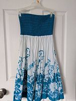Blue and white girls sundress with strapless elasticized bodice and floral print skirt hanging on white hanger against white door.
