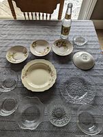 Overview of various glass bowls, ceramic plates with floral patterns, and a textured glass serving plate arranged on a table