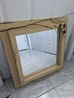 Front angled view of square distressed wooden frame mirror showing cream color, natural twig decoration, and star accents.