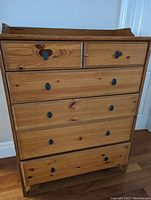 Front view showing the full dresser with six drawers visible and metal handles, natural pine wood with visible knots
